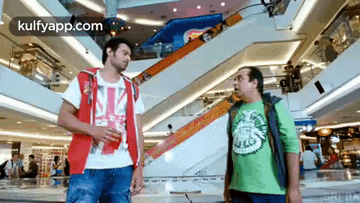 two men are standing in a mall talking to each other .