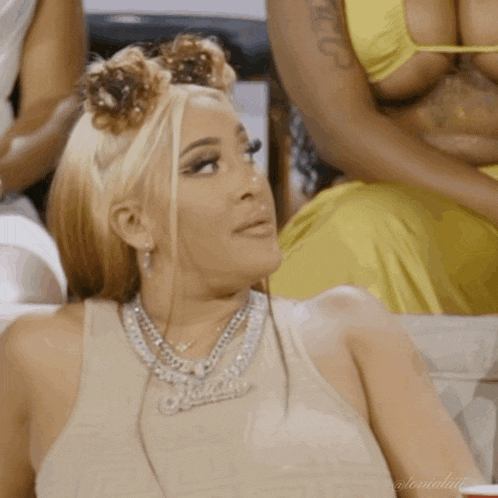 a woman wearing a tank top and a necklace with a name pendant is sitting on a couch