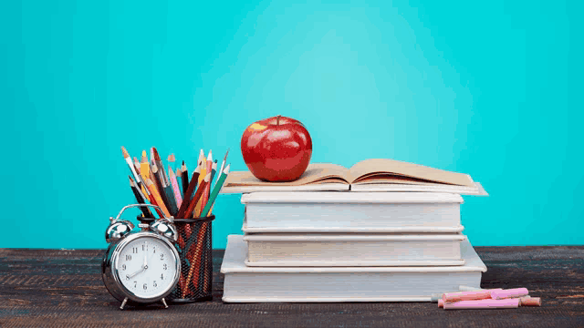 an apple sits on top of a stack of books next to a clock and pencils