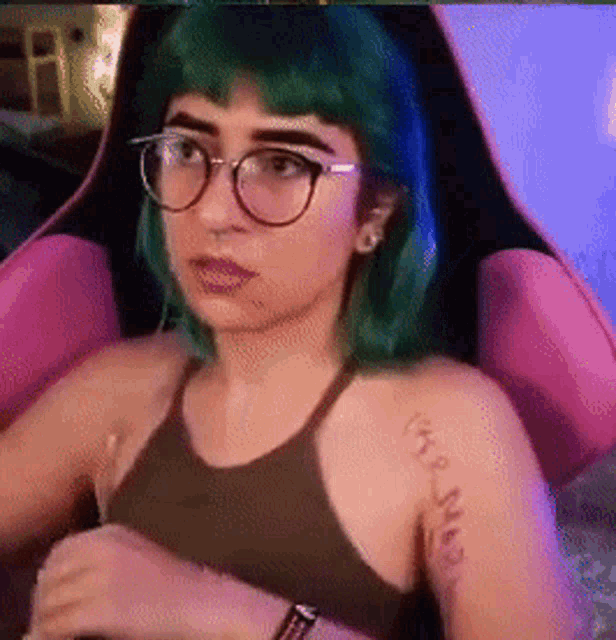 a girl with green hair and glasses is sitting in a pink chair .