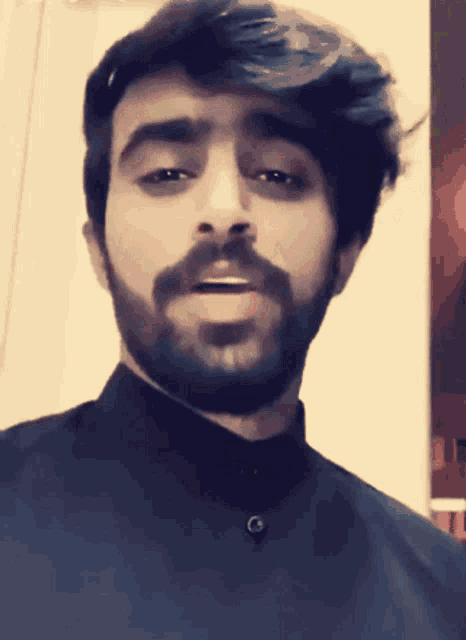 a man with a beard is wearing a black shirt with a button on the collar