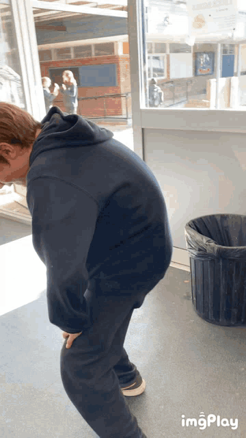 a man in a black hoodie is bending over next to a black trash can