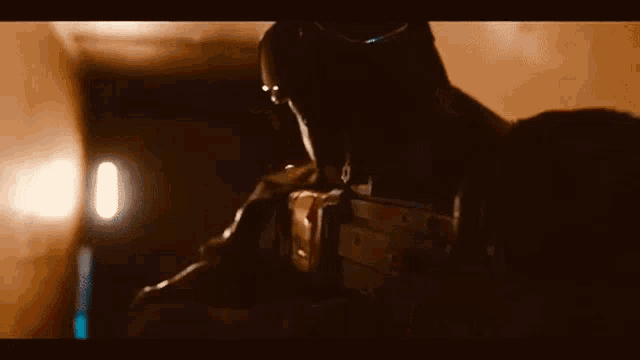 a man in a mask is holding a rifle in a dark room .
