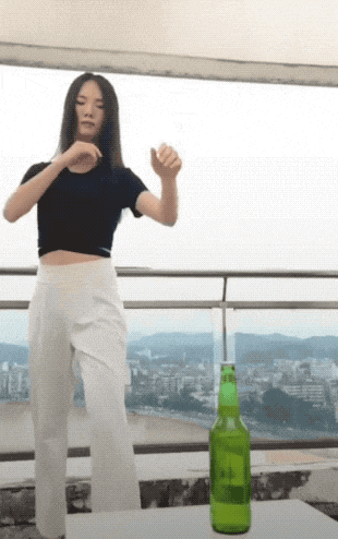 a woman in a black top and white pants is standing next to a bottle of beer