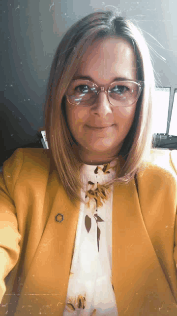 a woman wearing glasses and a yellow jacket is smiling for the camera