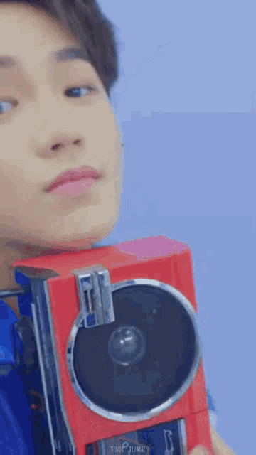 a man in a blue shirt is holding a red camera .
