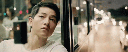 a man is sitting on a bus looking out the window at the city .
