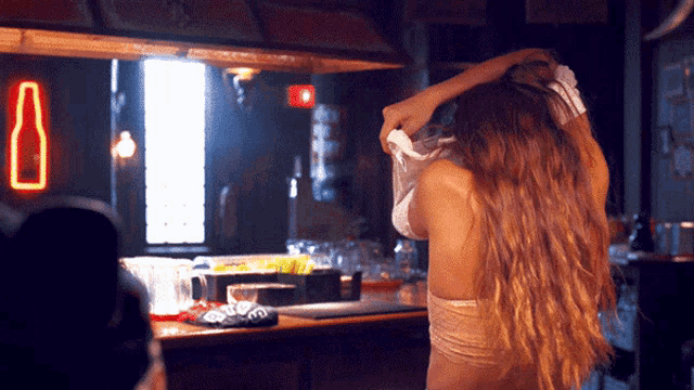 a woman takes off her shirt in front of a neon sign that says bottle