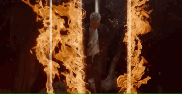 a man stands in front of a wall of flames