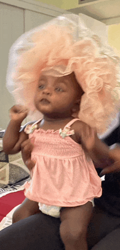 a little girl wearing a pink dress and a diaper is sitting on someone 's lap