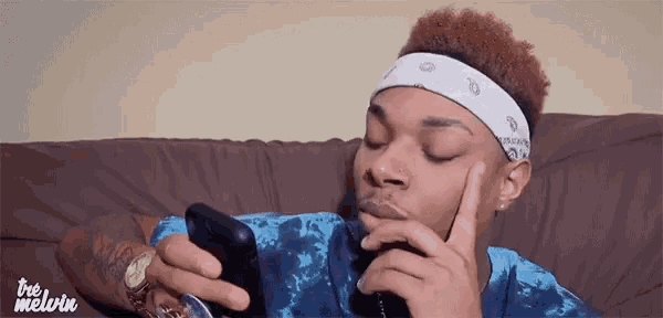 a young man is sitting on a couch looking at his cell phone .