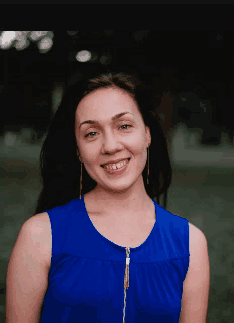 a woman wearing a blue top with a zipper on the front smiles for the camera