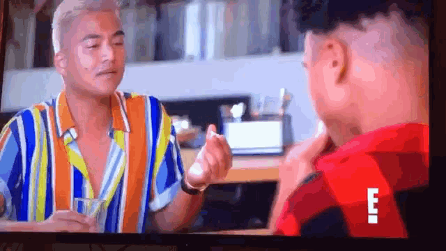 a man in a striped shirt is talking to another man in a red shirt .