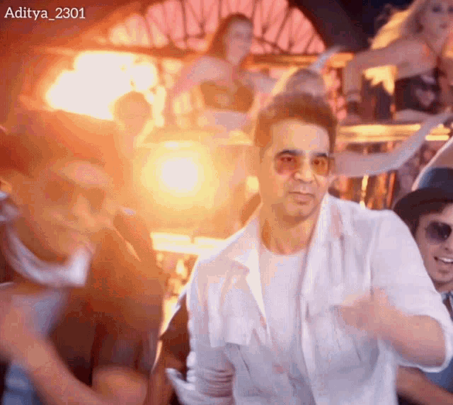 a man in a white shirt and sunglasses is dancing in front of a crowd of people .