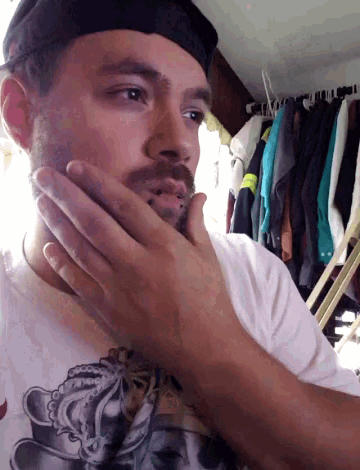 a man with a beard wearing a hat and a white shirt shaves his face