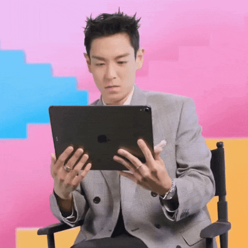 a man in a suit sits in a director 's chair holding an apple ipad