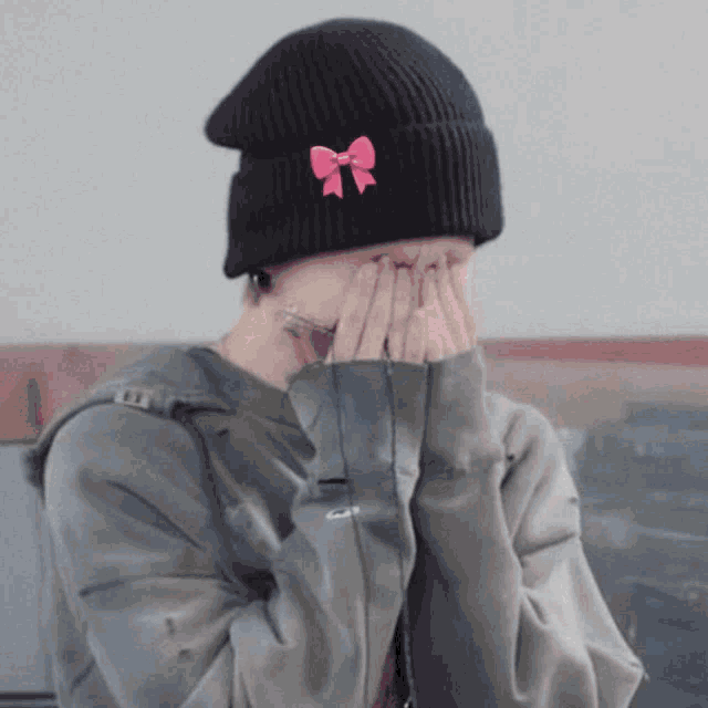 a person wearing a black hat with a pink bow on it covering their face