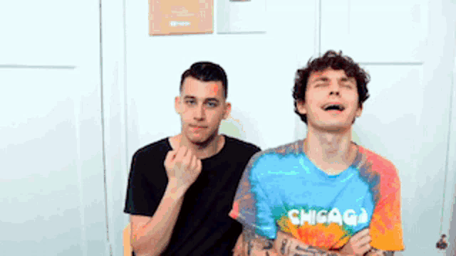 two men are sitting next to each other and one of them is wearing a tie dye shirt with the word chicago on it .