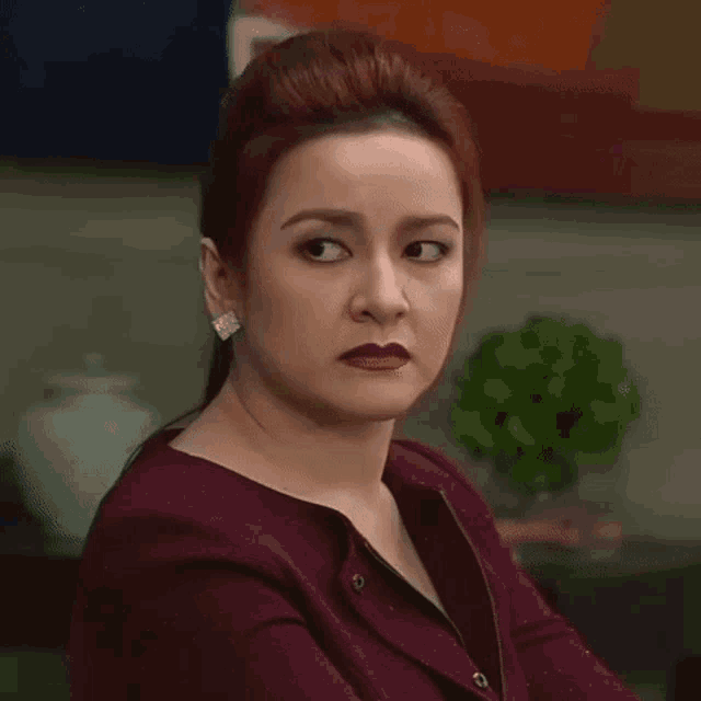 a woman with red hair is wearing a maroon jacket and earrings .