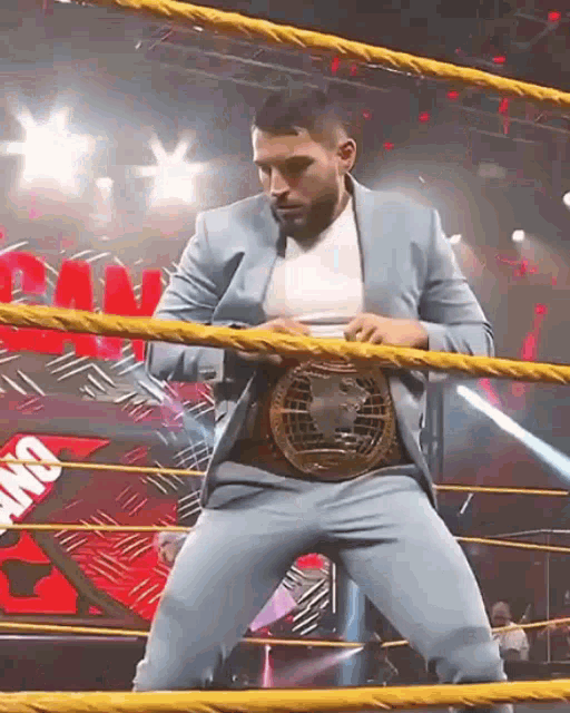 a man in a suit is standing in a wrestling ring holding a belt .