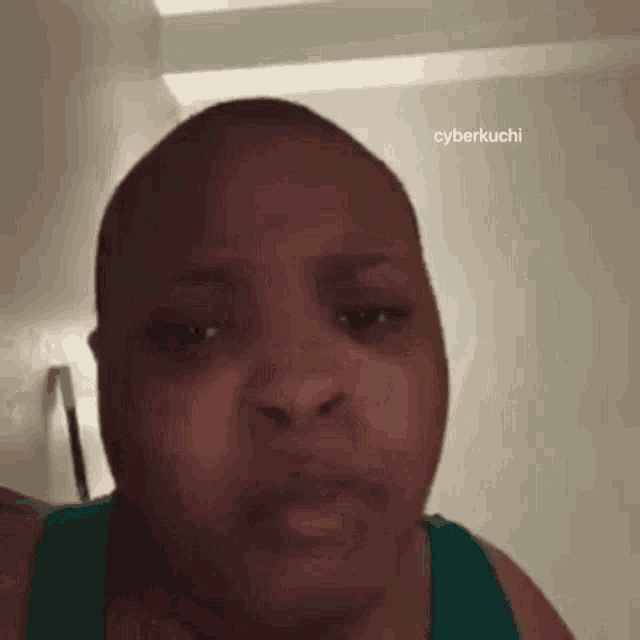 a woman with a shaved head is making a funny face while wearing a green tank top .