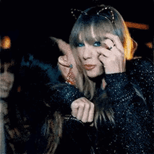 a woman with cat ears on her head is kissing another woman on the cheek .