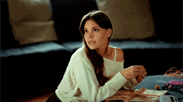 a woman in a white sweater is sitting on the floor in front of a table .