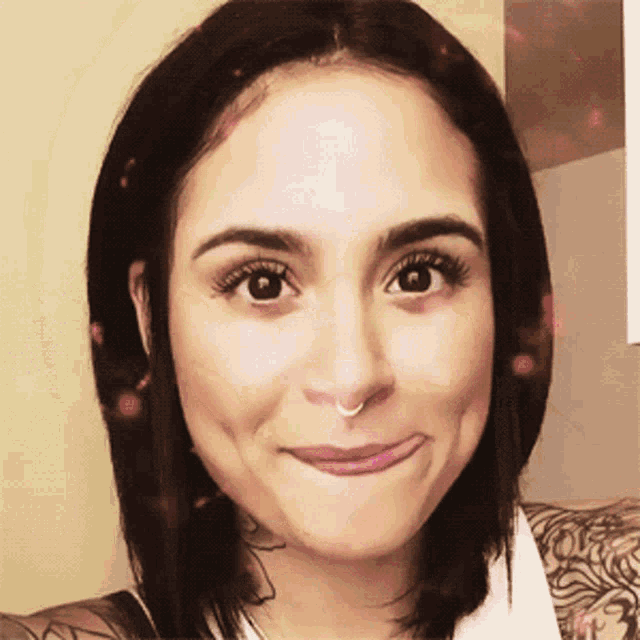 a woman with a nose ring is smiling and has a tattoo on her arm