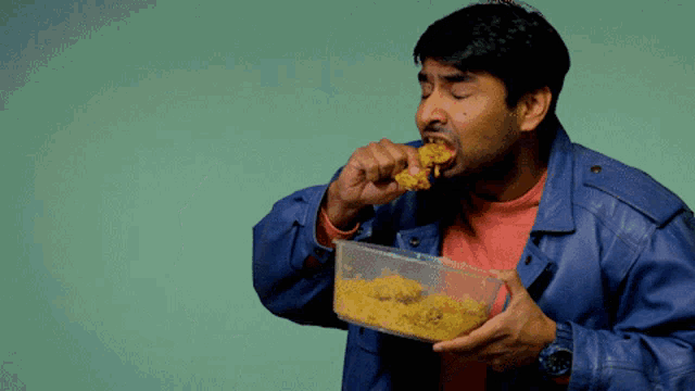 a man in a blue jacket is eating a piece of food from a plastic container
