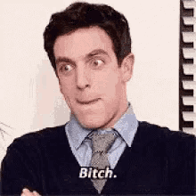 a man in a tie is making a funny face and saying bitch .