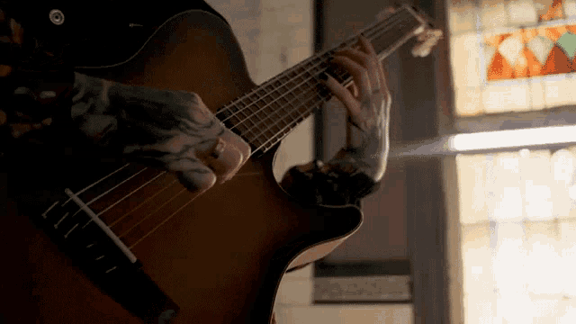 a man with tattoos is playing an acoustic guitar in front of a stained glass window .