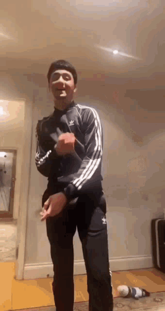 a man in a black adidas tracksuit is standing in a room .