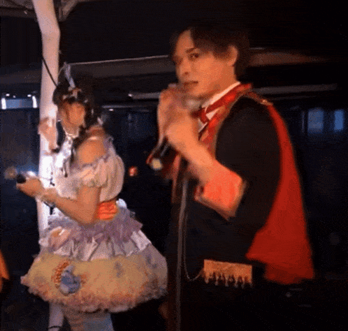 a man singing into a microphone next to a woman in a costume