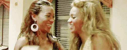 two women are standing next to each other and laughing in front of a window .