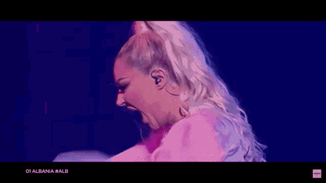 a woman in a white dress is dancing on a stage in front of a blue and pink background .