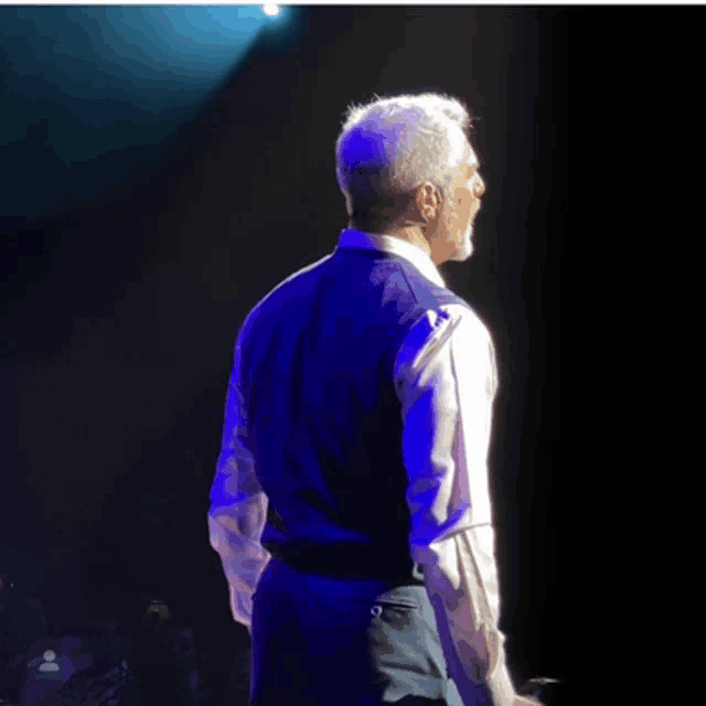 a man in a white shirt and a blue vest is standing in front of a blue light