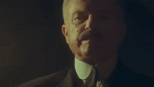 a man in a suit and tie is talking to someone in a dark room .