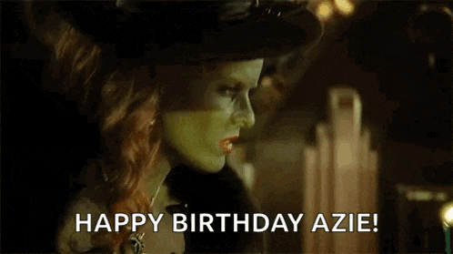a woman with green paint on her face is blowing out a candle on a cupcake and saying `` happy birthday azie '' .