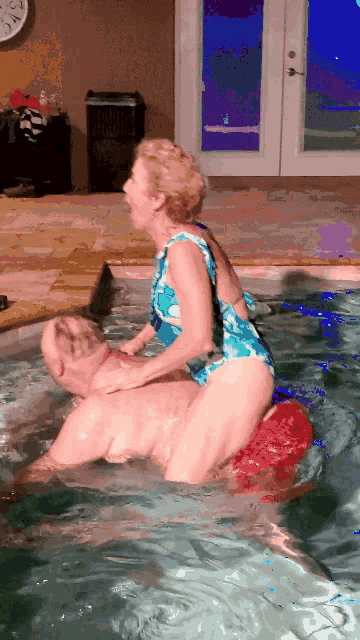 a woman in a blue bathing suit sits on a man in a pool