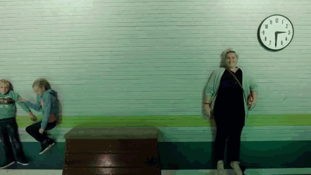 a woman stands in front of a wall with a clock on it that shows the time as 7:10