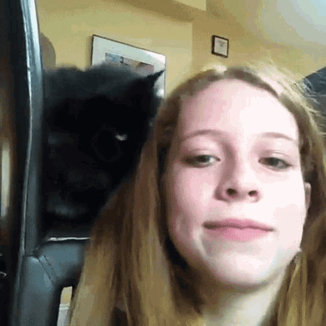 a woman taking a selfie with a black cat on her head