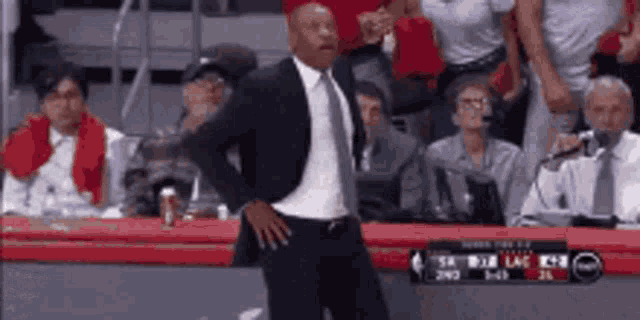a man in a suit and tie is standing in front of a crowd of people at a basketball game .