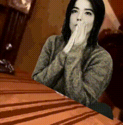 a woman in a sweater sits at a table with her hands on her face