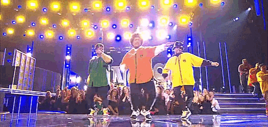 a group of people are dancing on a stage in front of a crowd with the word tnt in the background .