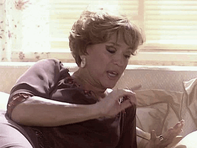 a woman is sitting on a couch making a funny face while holding something in her hand .