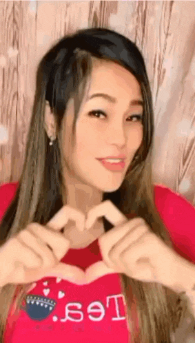 the woman is wearing a red shirt and making a heart shape with her hands .