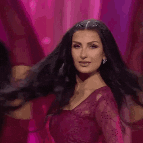 a woman with long black hair and earrings is wearing a red dress and looking at the camera .