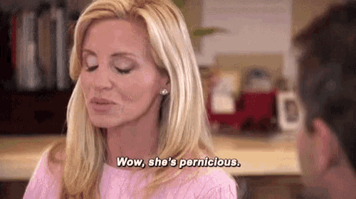 a woman in a pink sweater is talking to a man in a kitchen and saying wow , she 's perilous .