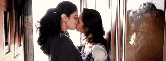 two women are kissing each other in front of a window .