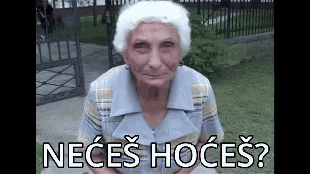 an elderly woman with white hair is sitting in front of a fence and making a funny face .